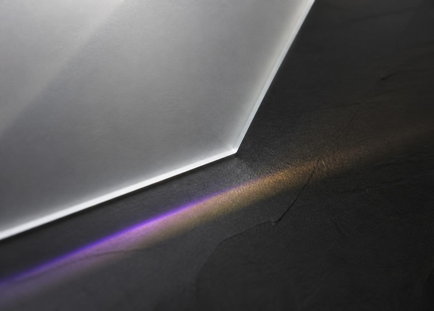 Light refracting along the edge of a frosted glass plane on dark stone